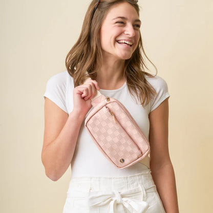 person wearing white pants and top with blush Urban Check Belt Bag across their chest.