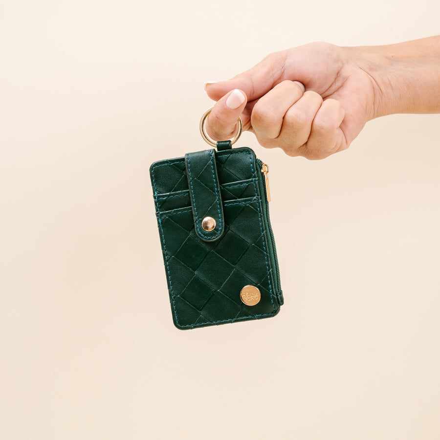 handing with finger looped through ring of green woven keychain wallet.