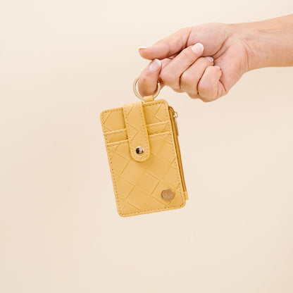 handing with finger looped through ring of mustard woven keychain wallet.