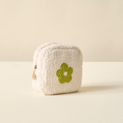 white sherpa pouch with green flower on it set on an off-white table.