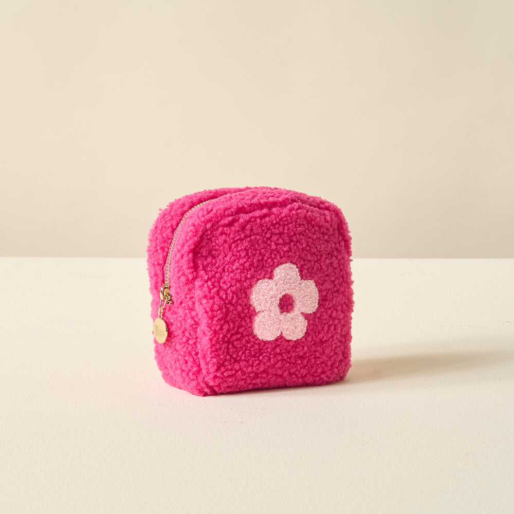 hot pink sherpa zipper pouch with pink flower on it set on an off-white table.