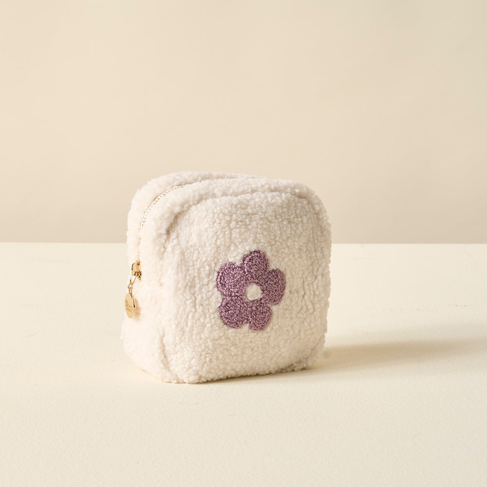 white sherpa pouch with purple flower on it set on an off-white table.
