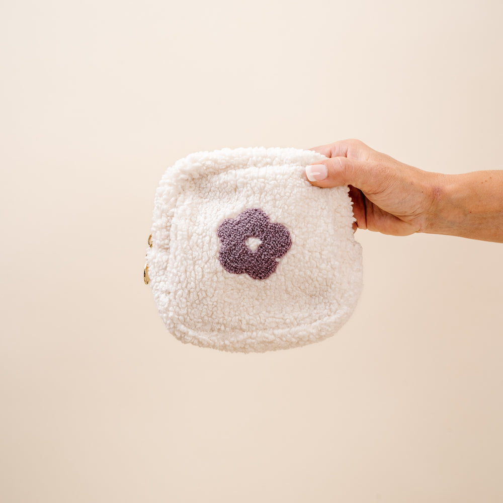 hand holding white sherpa pouch with purple flower in it.
