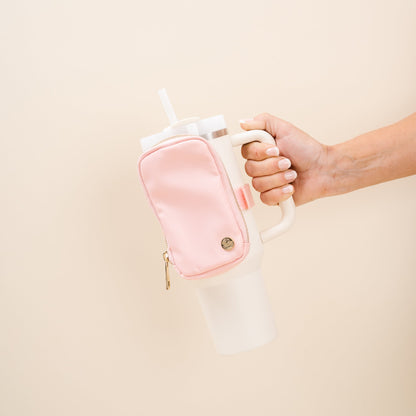 hand holding a tumbler with a blush tumbler fanny pack strapped to it.