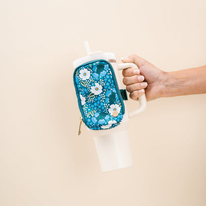 hand holding a tumbler with a blue floral tumbler fanny pack strapped to it.