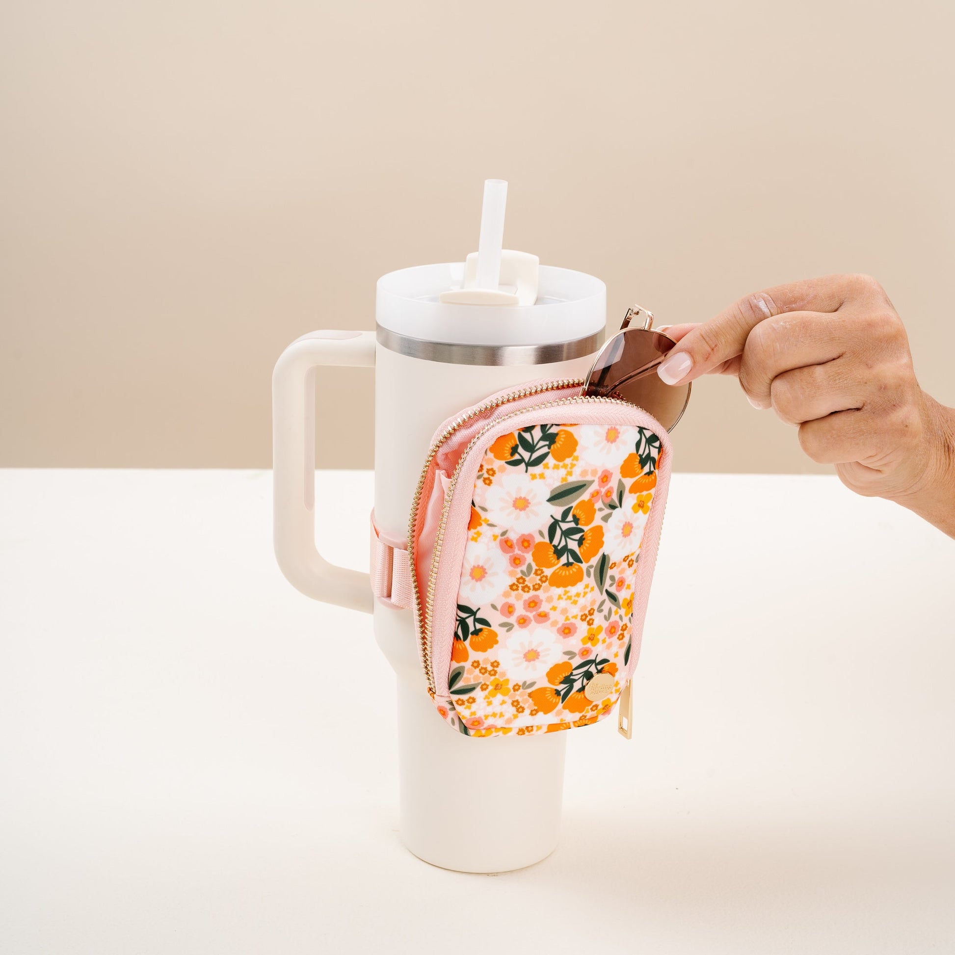 hand putting sunglasses in a orange and pink floral tumbler fanny pack strapped to a tumbler.