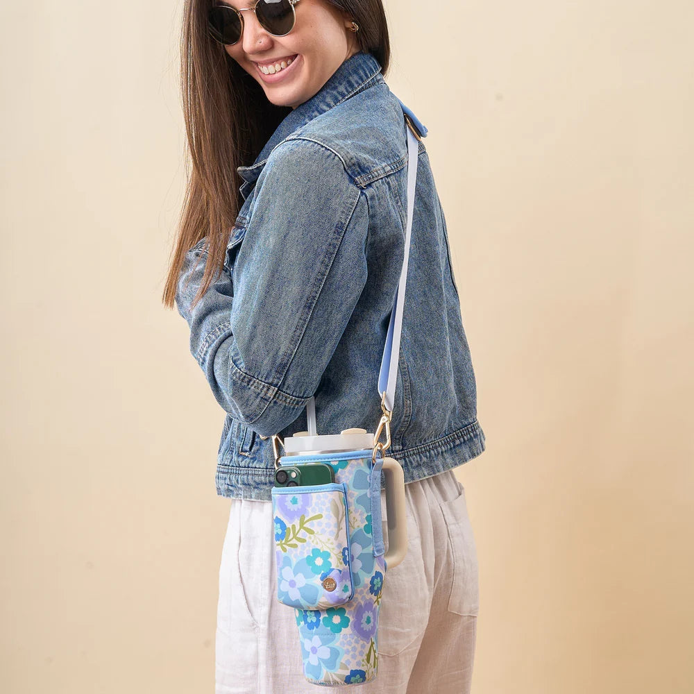 person wearing khaki pants and denim jacket with blue and green blooms tumbler sling across their shoulder.