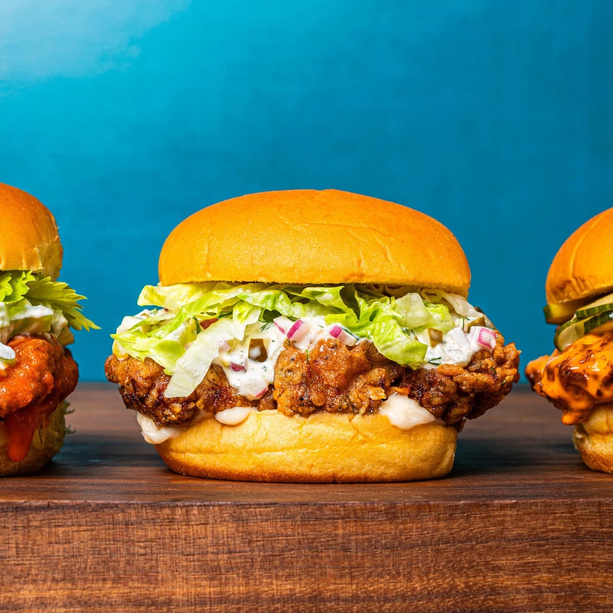 sandwich on a bun with lettuce, sauce, and meat filling set on a wooden surface