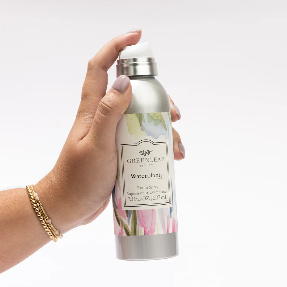 Hand holding a mister bottle of waqterplants Greenleaf room spray bottle with floral design on a white background