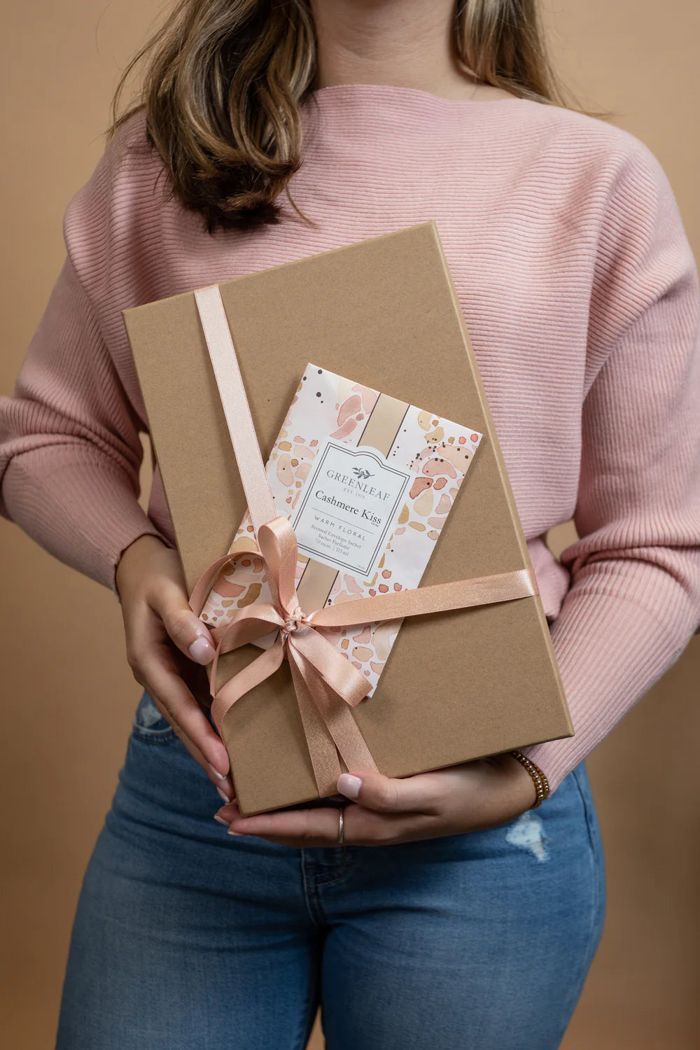 person holding a wrapped gift with a Cashmere Kiss Large Sachet slipped under the ribbon