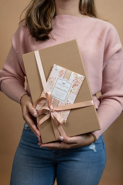 person holding a wrapped gift with a Cashmere Kiss Large Sachet slipped under the ribbon