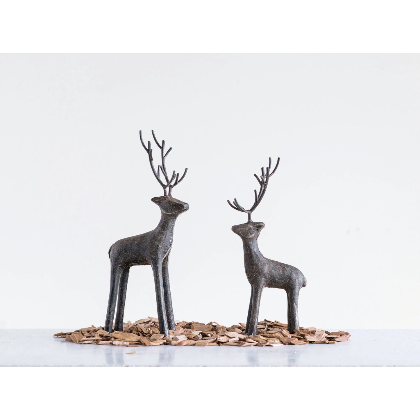 2 sizes of metal deer arranged on a  table with bits of bark around their feet.