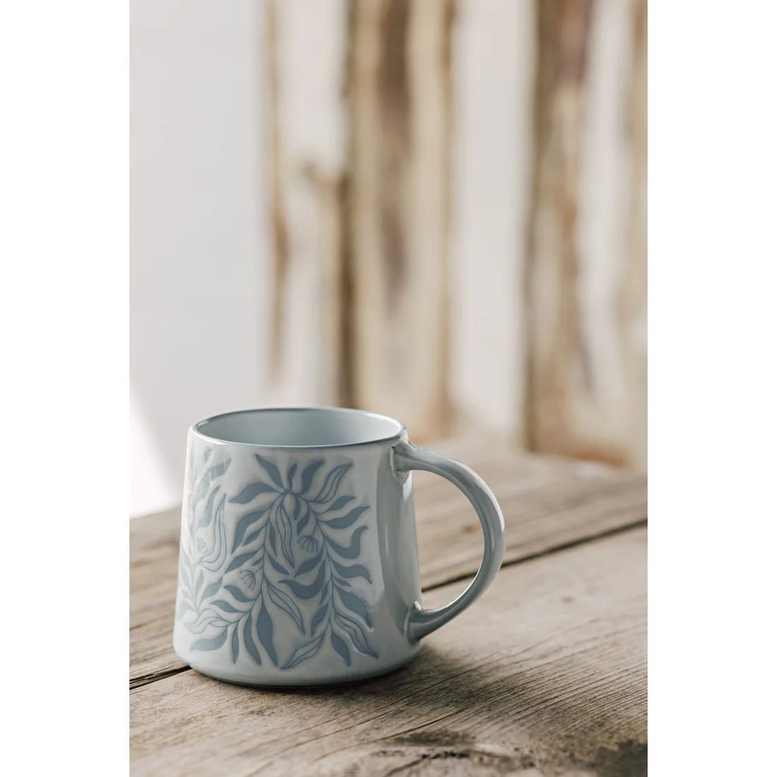 White ceramic mug with blue floral pattern on a wooden surface