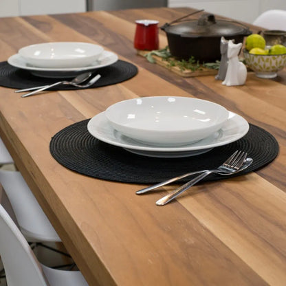 Dining table set with white plates, black placemats, and silverware on a wooden surface.