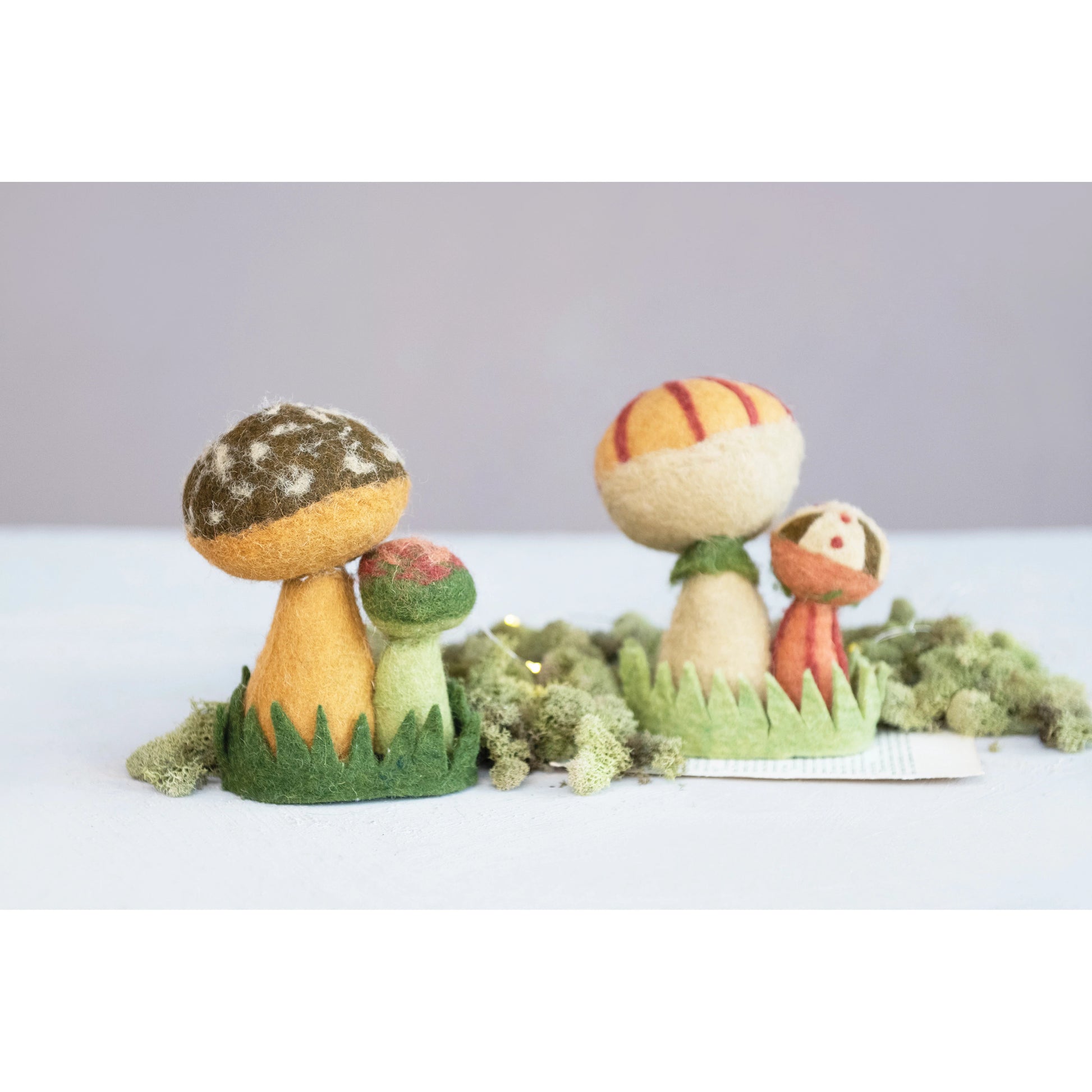 both styles of wool felt mushrooms displayed on a green surface surrounded by moss