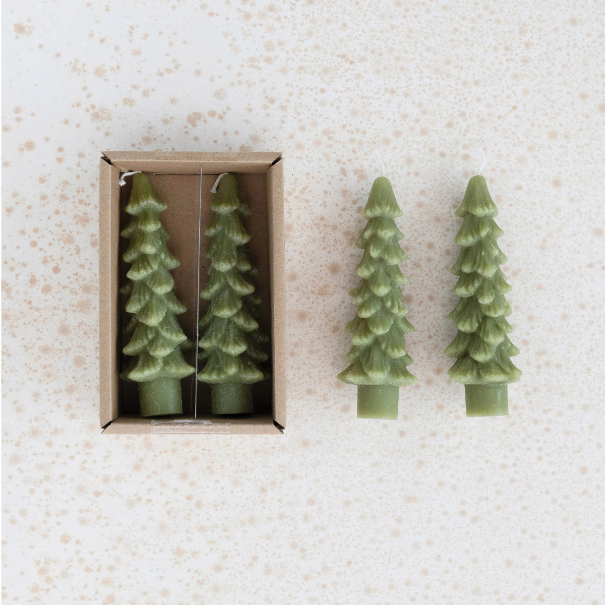 green tree shaped taper candles in the box with 2 other candles laying next to it on a gold speckled background.