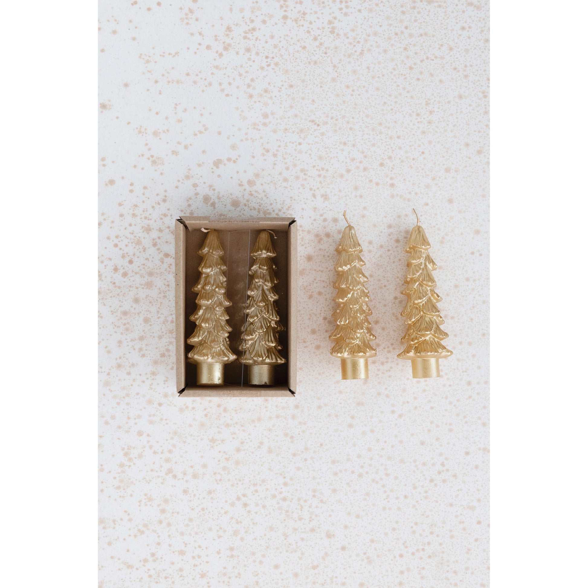 gold tree shaped taper candles in the box and 2 others next to the box on a gold speckled background.