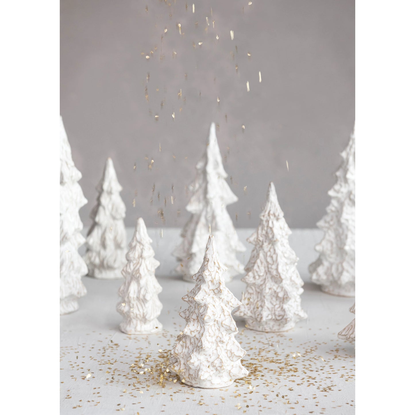 several sizes and shapes of stoneware trees arranged on a table with gold confetti sprinkle around.