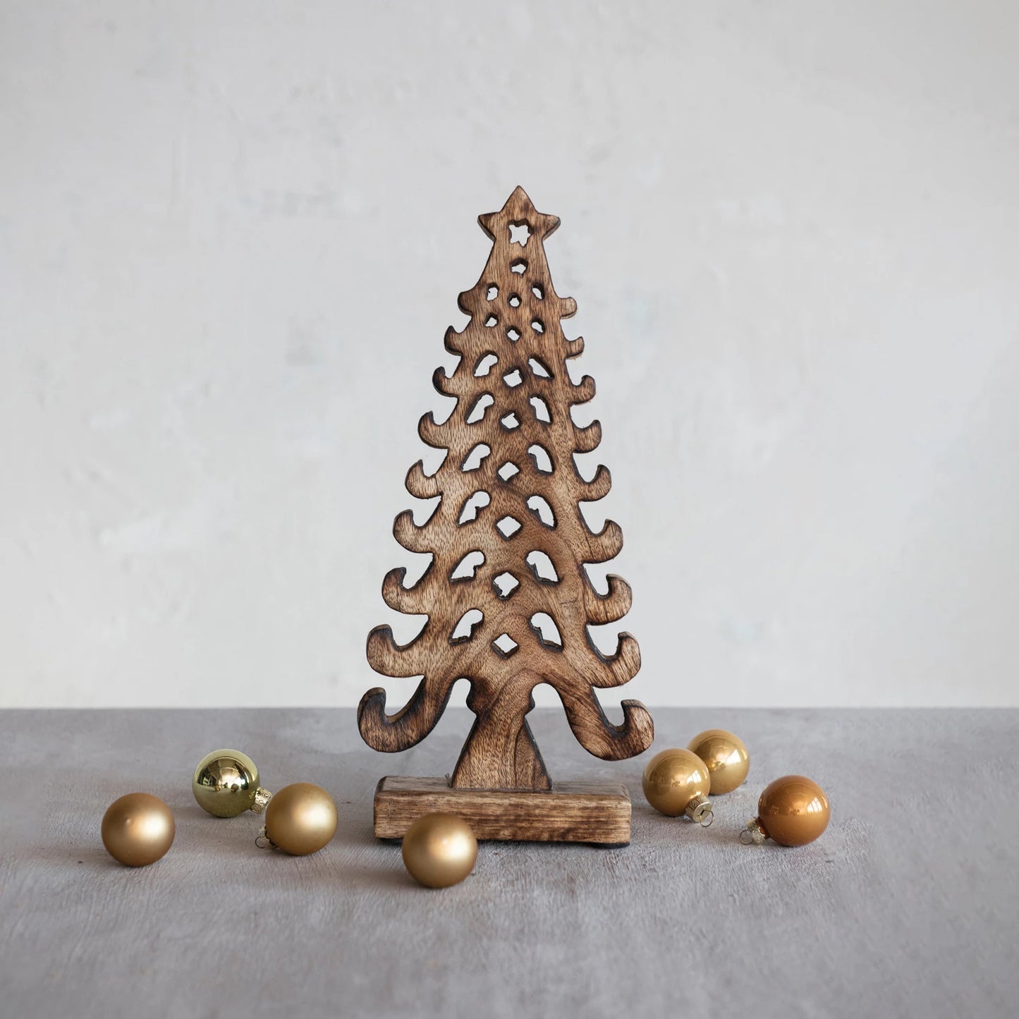 cut-out wooden tree standing on a grey table with gold ornament balls scattered around.