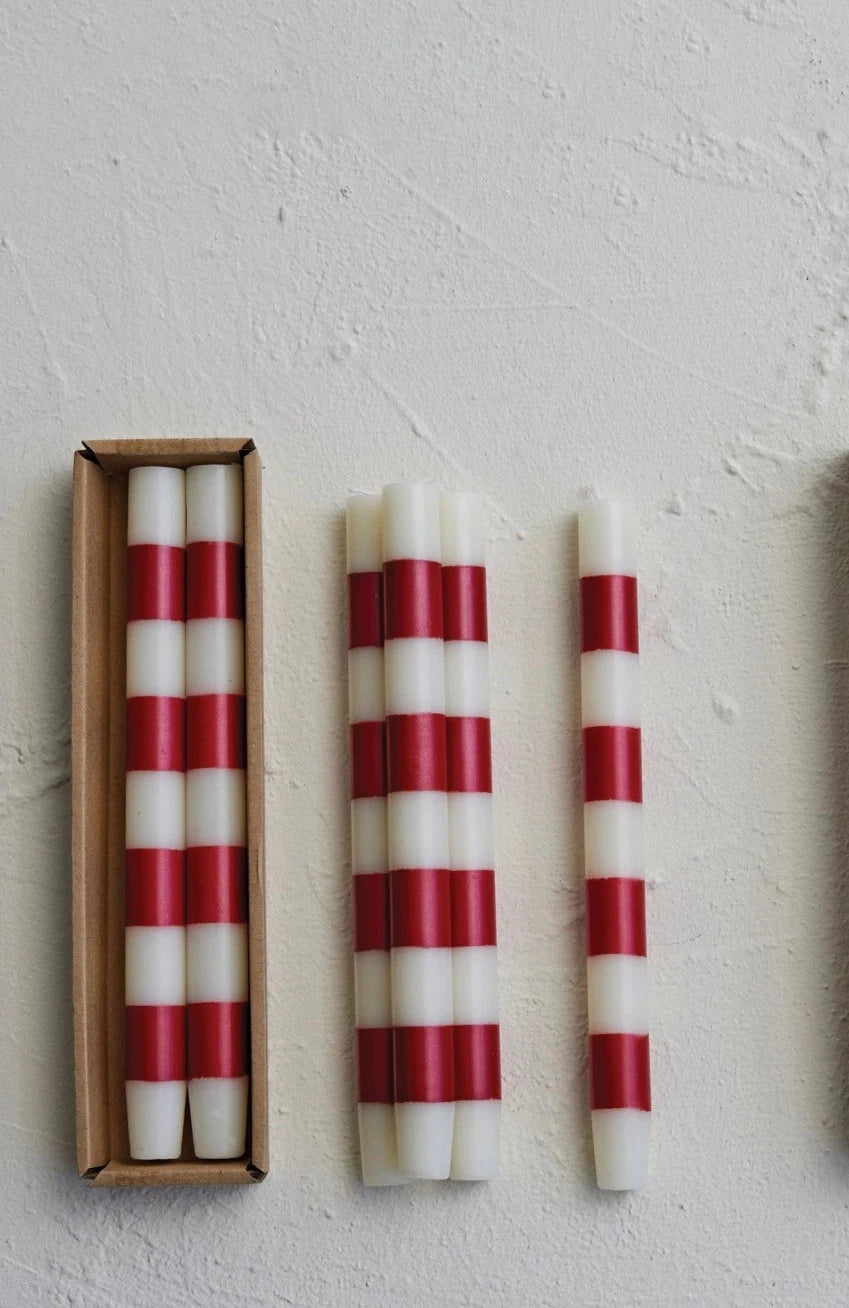 red and white striped candles, some in box, others piled next to it, arranged on a plaster background.