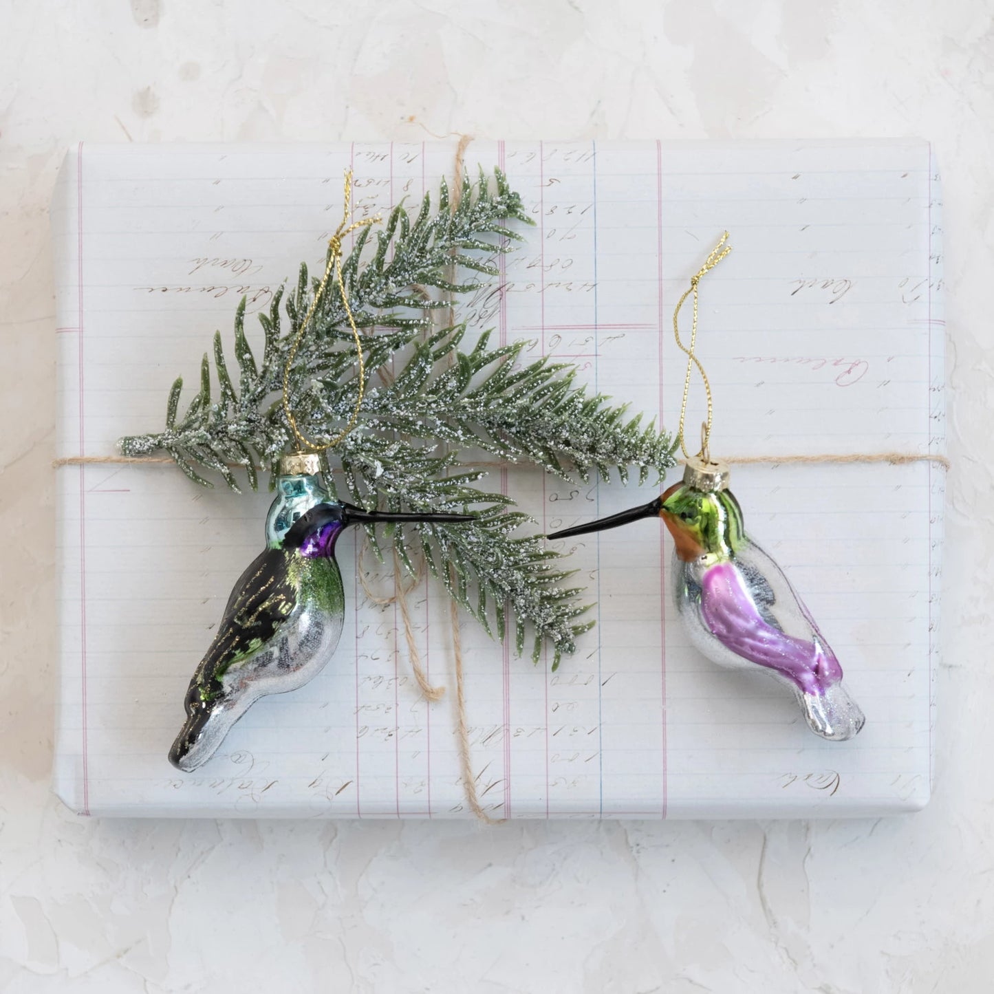 2 colors of hummingbird ornaments arranged with a sprig of greenery.