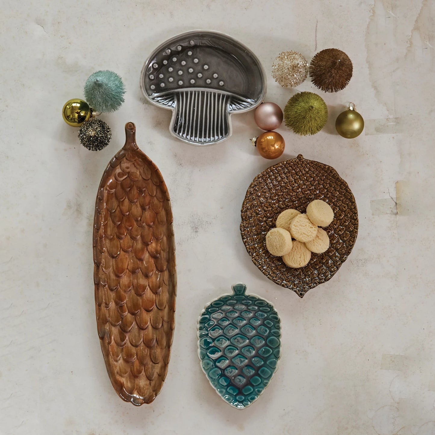top view of the pinecone shaped stoneware cracker dish displayed next to two othe pinecone shaped dishes and a mushroom shaped dish, bottle brush trees and ornaments