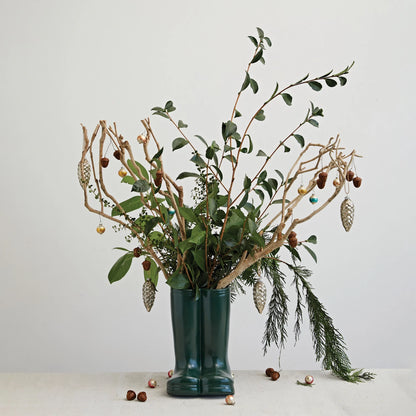 stoneware garden boot vase filled with branches, pine sprigs with pinecones and small acorns scattered all around