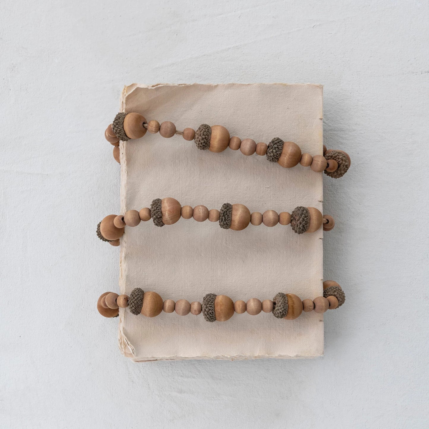 paulownia wood acorn and bead garland wrapped around a stack of recycled paper and displayed on a light surface