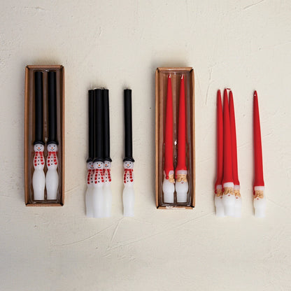 several sets of Santa and snowman candles, some in boxes, others piled next to the boxes, all arranged on a plaster background.