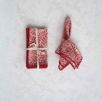 set of four red, white, and gold cotton napkins folded and tied with white string and displayed next to one in a napkin ring