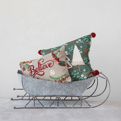 trees embroidered cotton slub pillow with pom poms displayed with the believe pillow in a tin sled