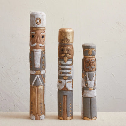 Three styles of mango wood nutcrackers set on a table with a plaster background.