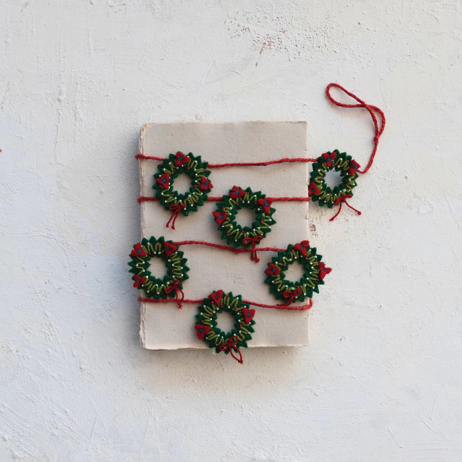 wreath garland wrapped around a stack of paper set on a plaster background.