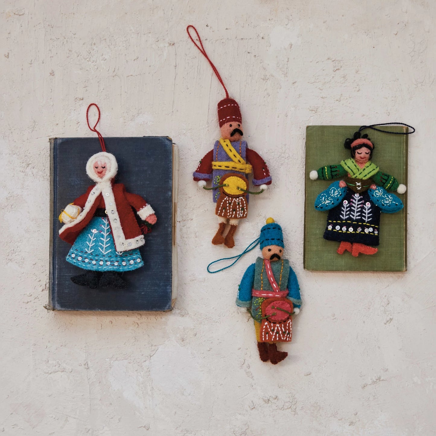 4 assorted styles of felt doll ornaments arranged on a plaster surface.