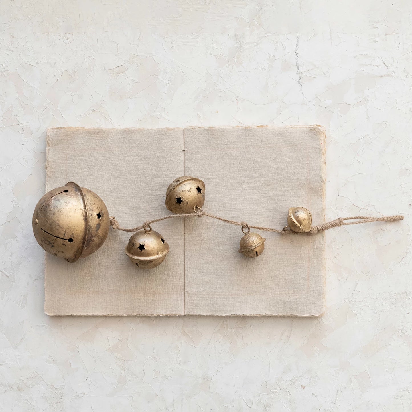 strand of gold bells on jute twine laying across a stack of papers on a plaster surface.