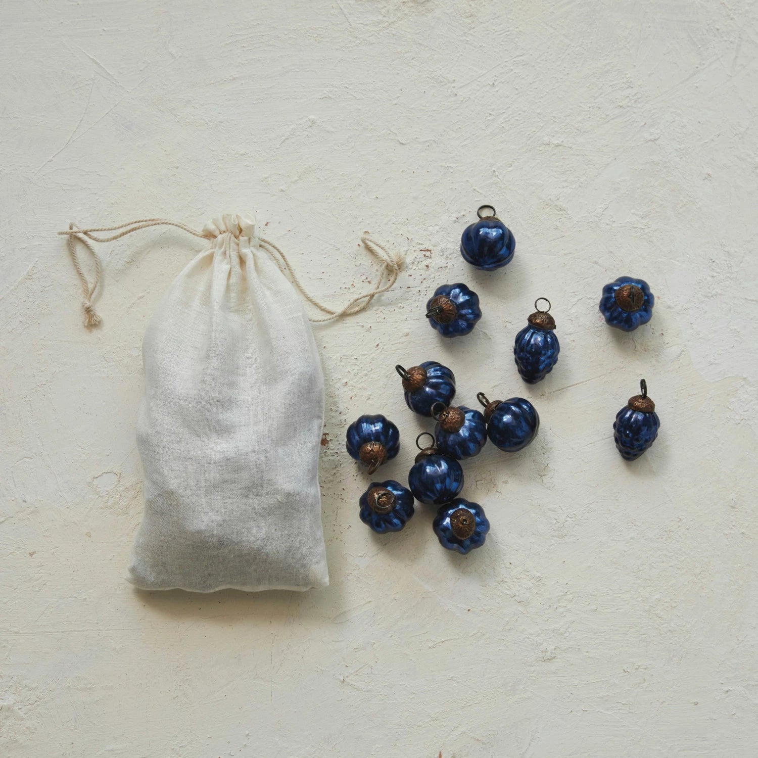 bag of ornaments wth several blue glass ornaments scattered around it set on a plaster background.