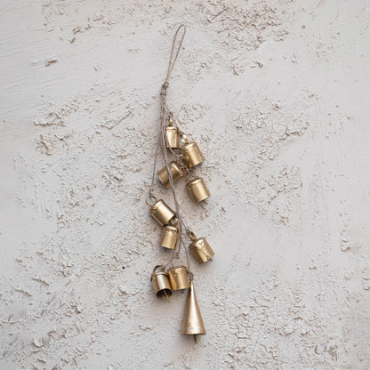 small gold bell tied together with jute rope draped across a plaster background.