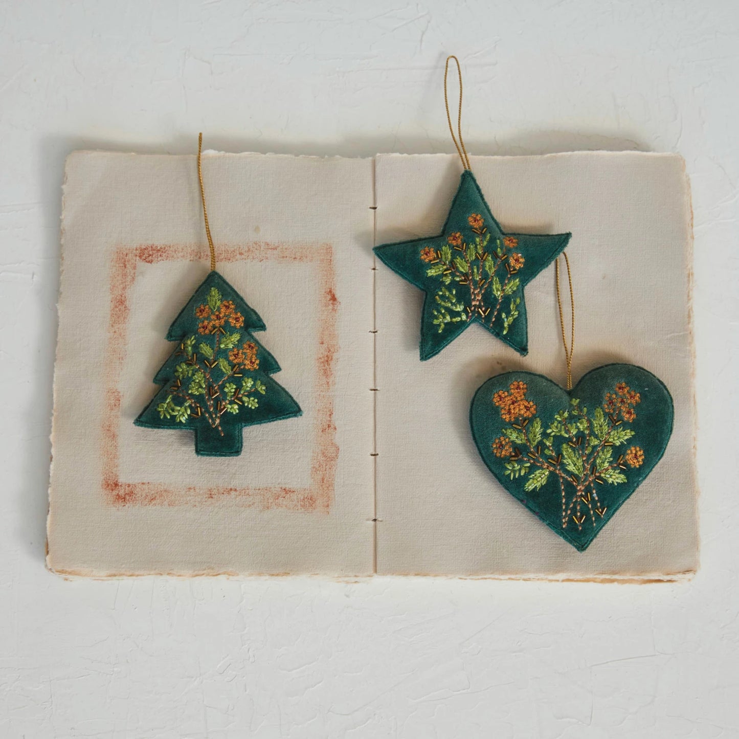 3 shapes of velvet beaded ornaments arranged on an open book.