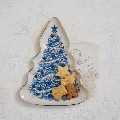 Tree shaped platter with blue. tree design and gold rim Set on a stack of papers with holiday cookies on it.