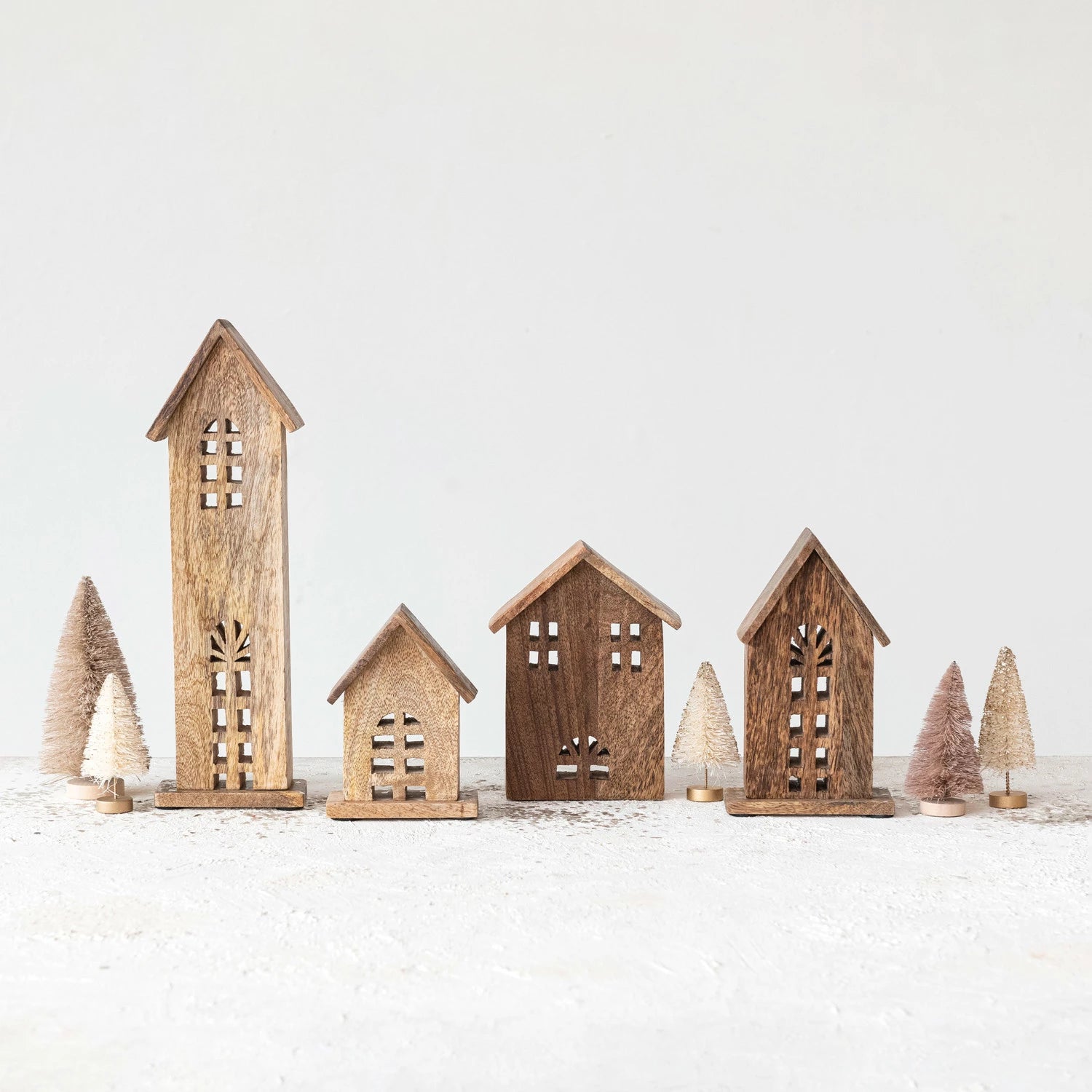 4 assorted sizes of wooden houses arranged on a table with little bottle brush trees.