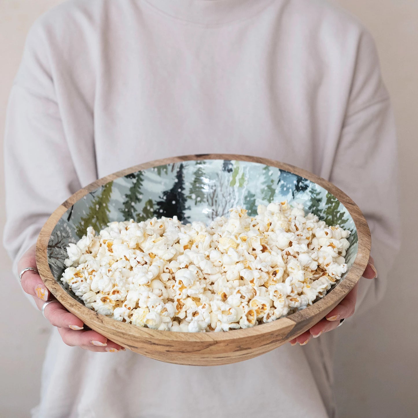 person holding wooden bowl with tree design filled with popcorn.