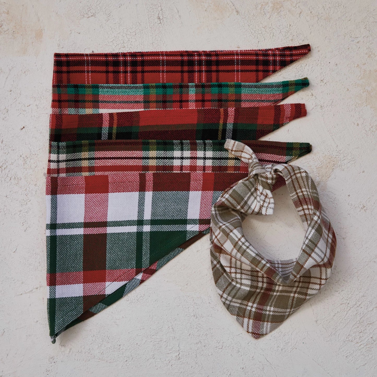 assorted plaid dog bandanas arranged on a plaster surface with one tied in a loop.