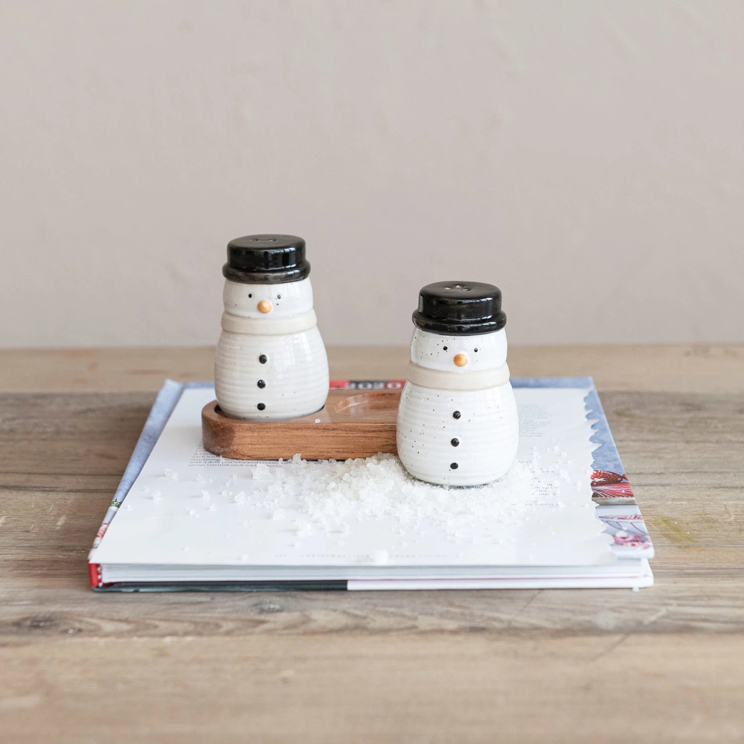 Snowmen salt and pepper shakers set on a book with salt scattered about.