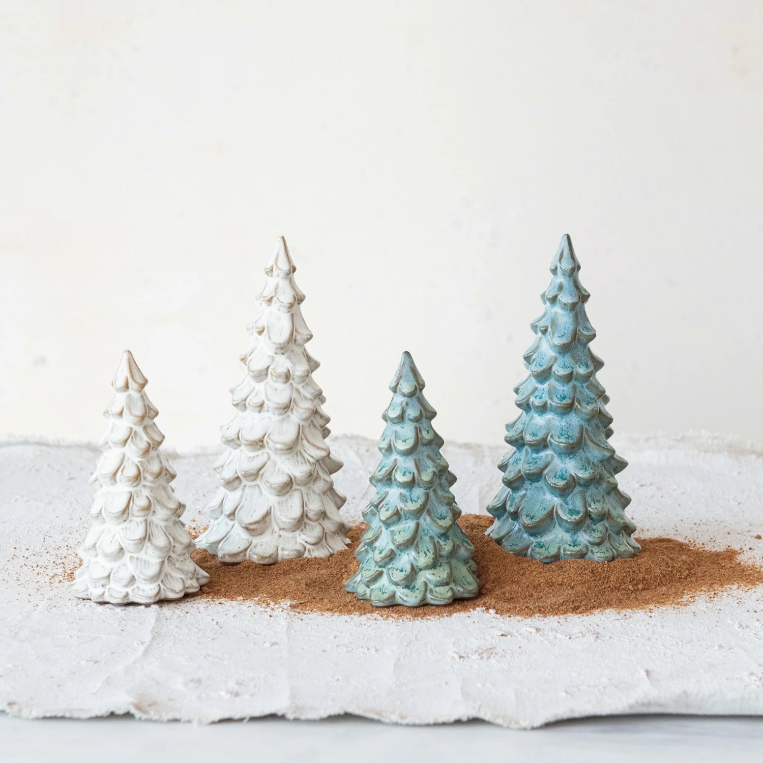 4 sizes and colors of stoneware trees arranged on a table with paper and sand.