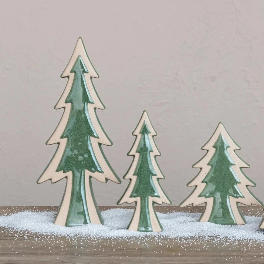 3 sizes of stoneware trees arranged on a table with artificial snow sprinkled around them.