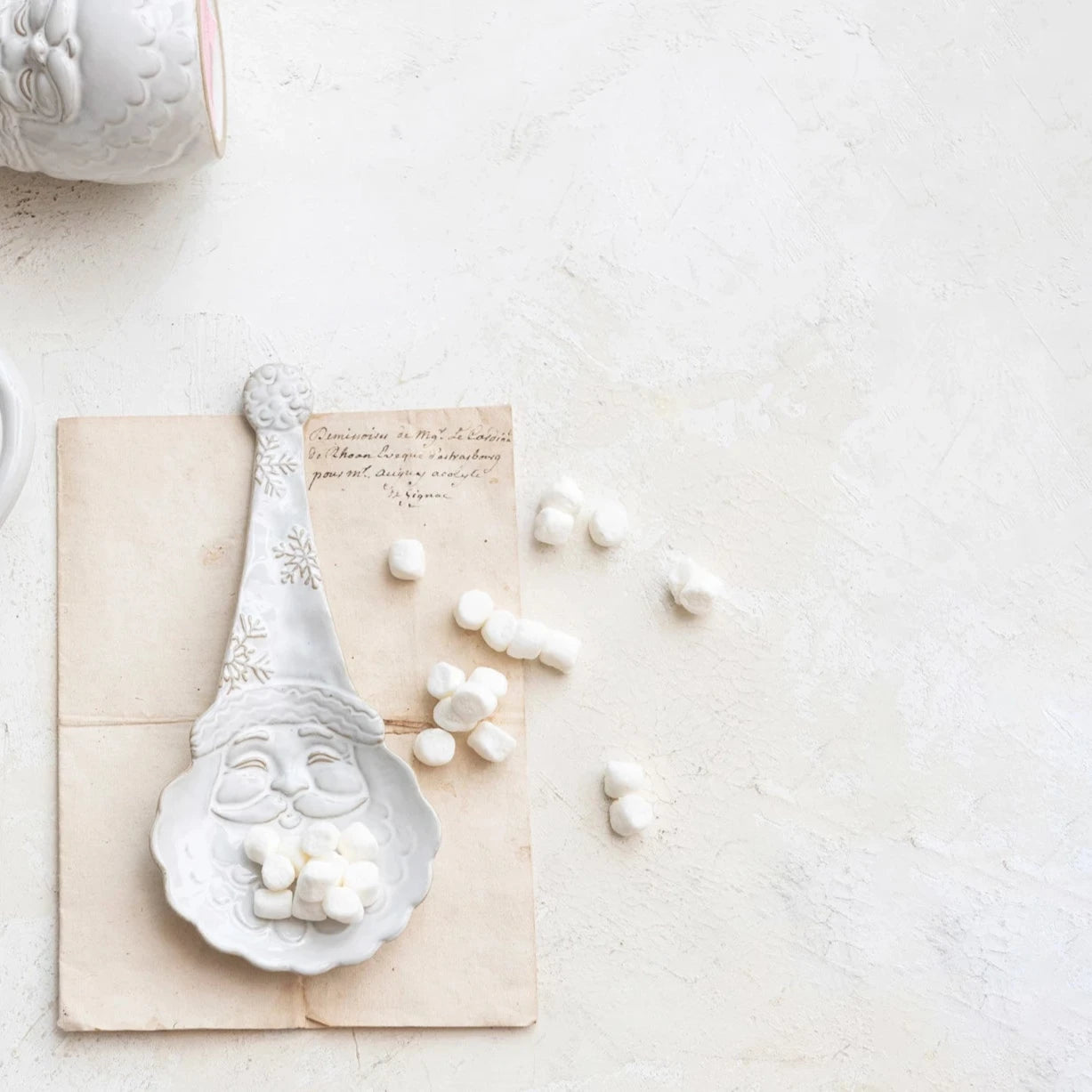 santa shaped spoon rest set on a bit of paper with marshmallows acattereda bout.