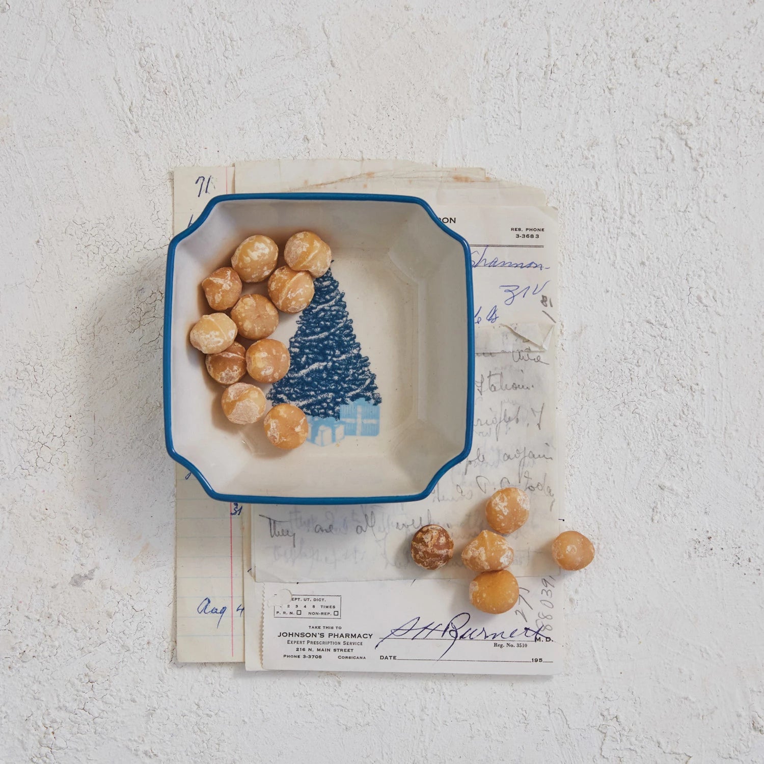 Bowl with tree design in the bottom and a blue rim set on a stack of papers and filled with treats.