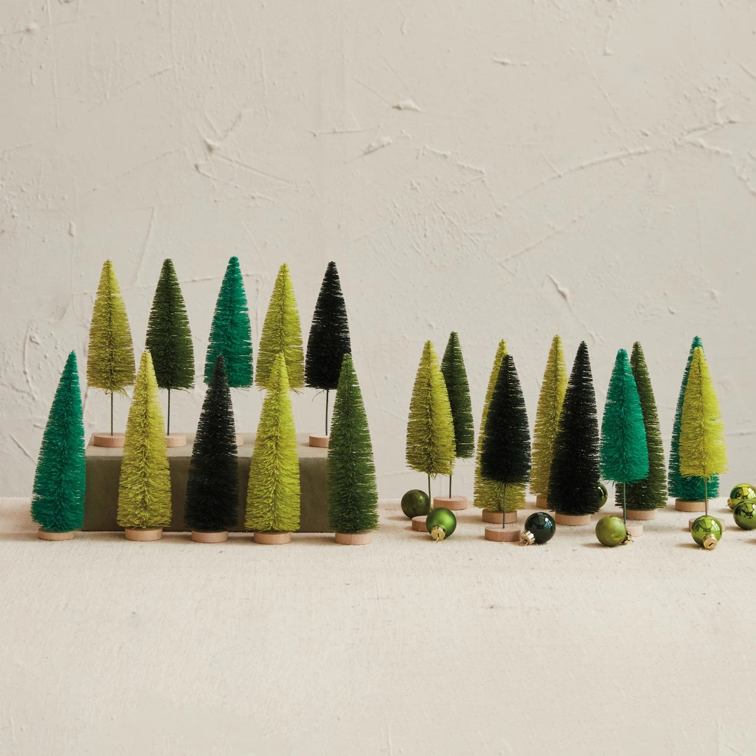 bottle brush trees in assorted colors and style arranged on a table with small ball ornaments.