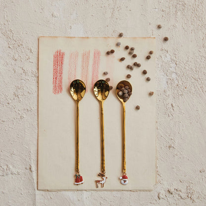 3 styles of holiday charm spoons arranged on a plaster surface with bits of spices.