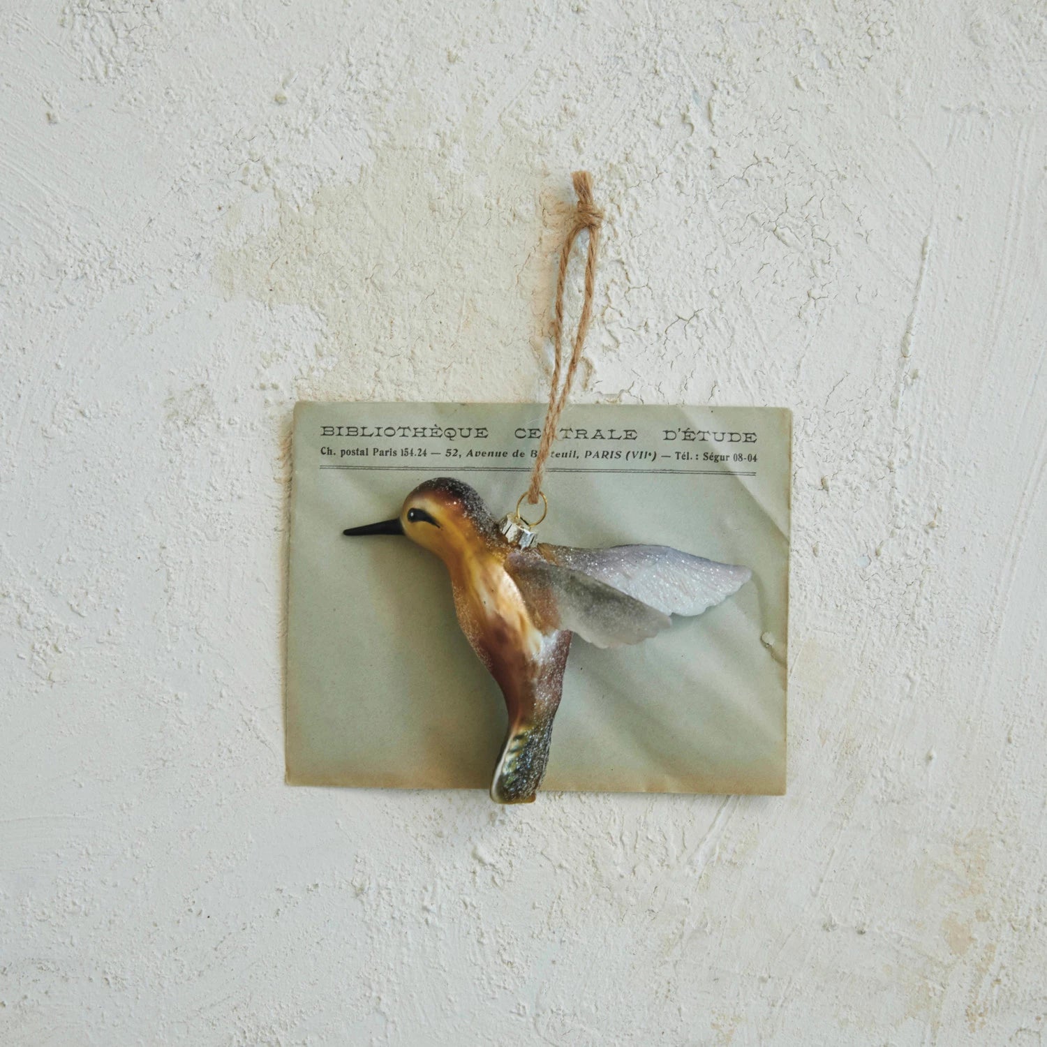 golden hummingbird ornament laying on a bit of paper.